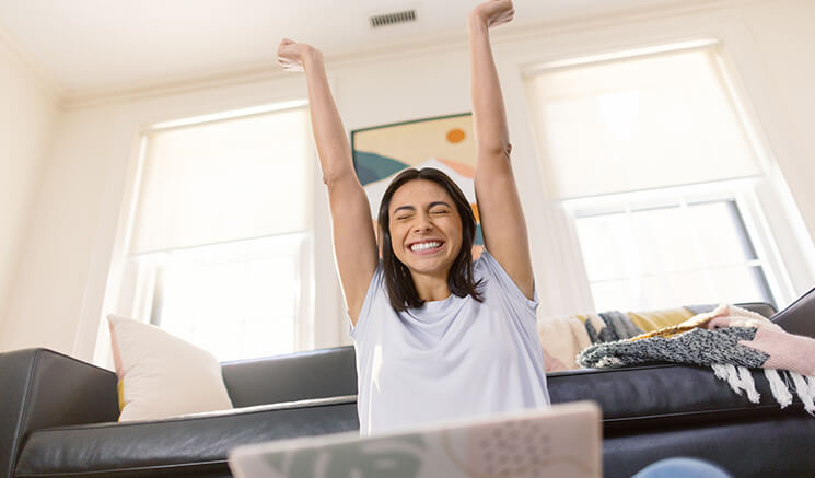 Female student sitting in front of laptop with arms raised and smiling